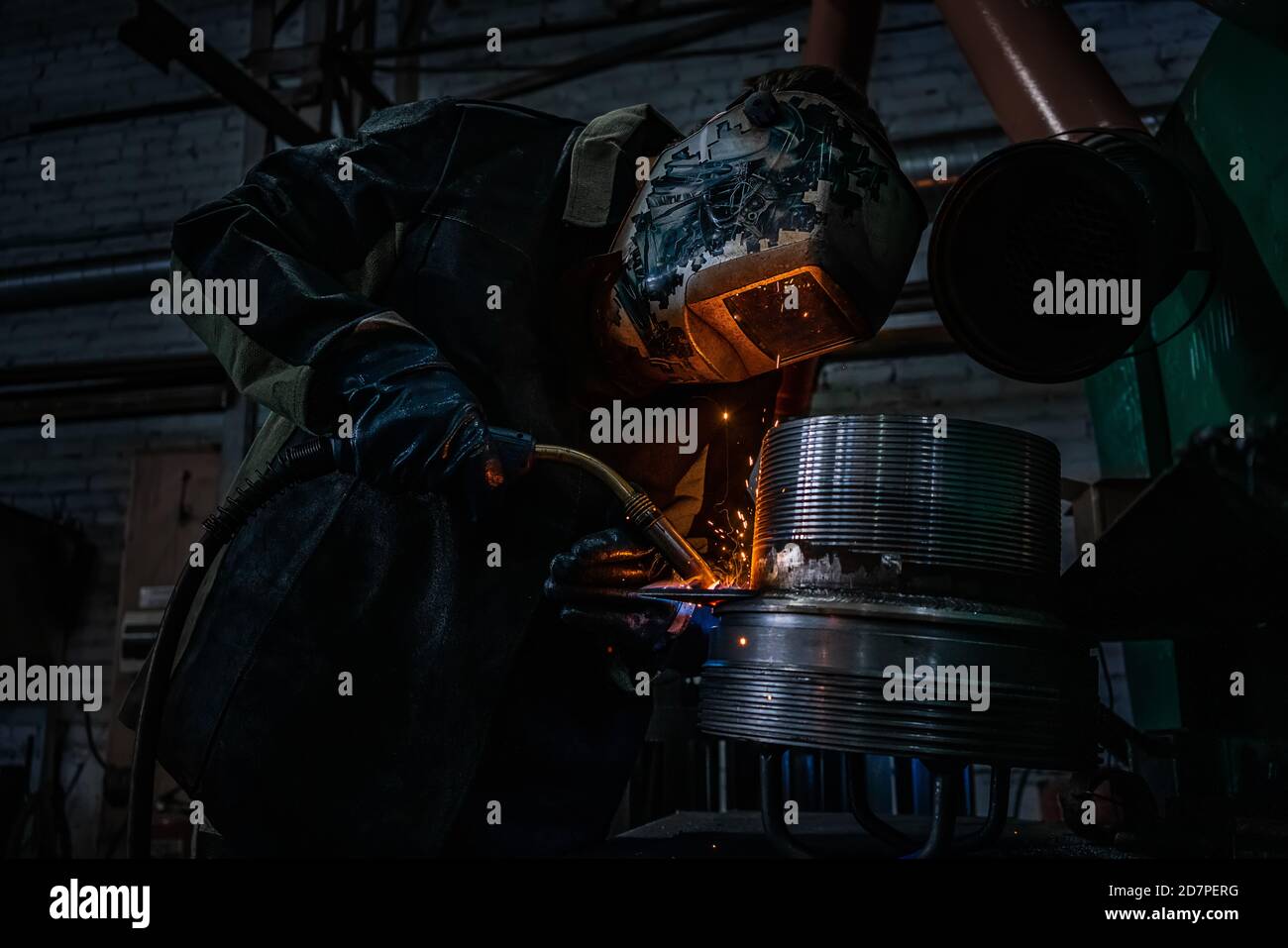 Side view of welder in protective helmet welding metal detail with sparks at factory Stock Photo