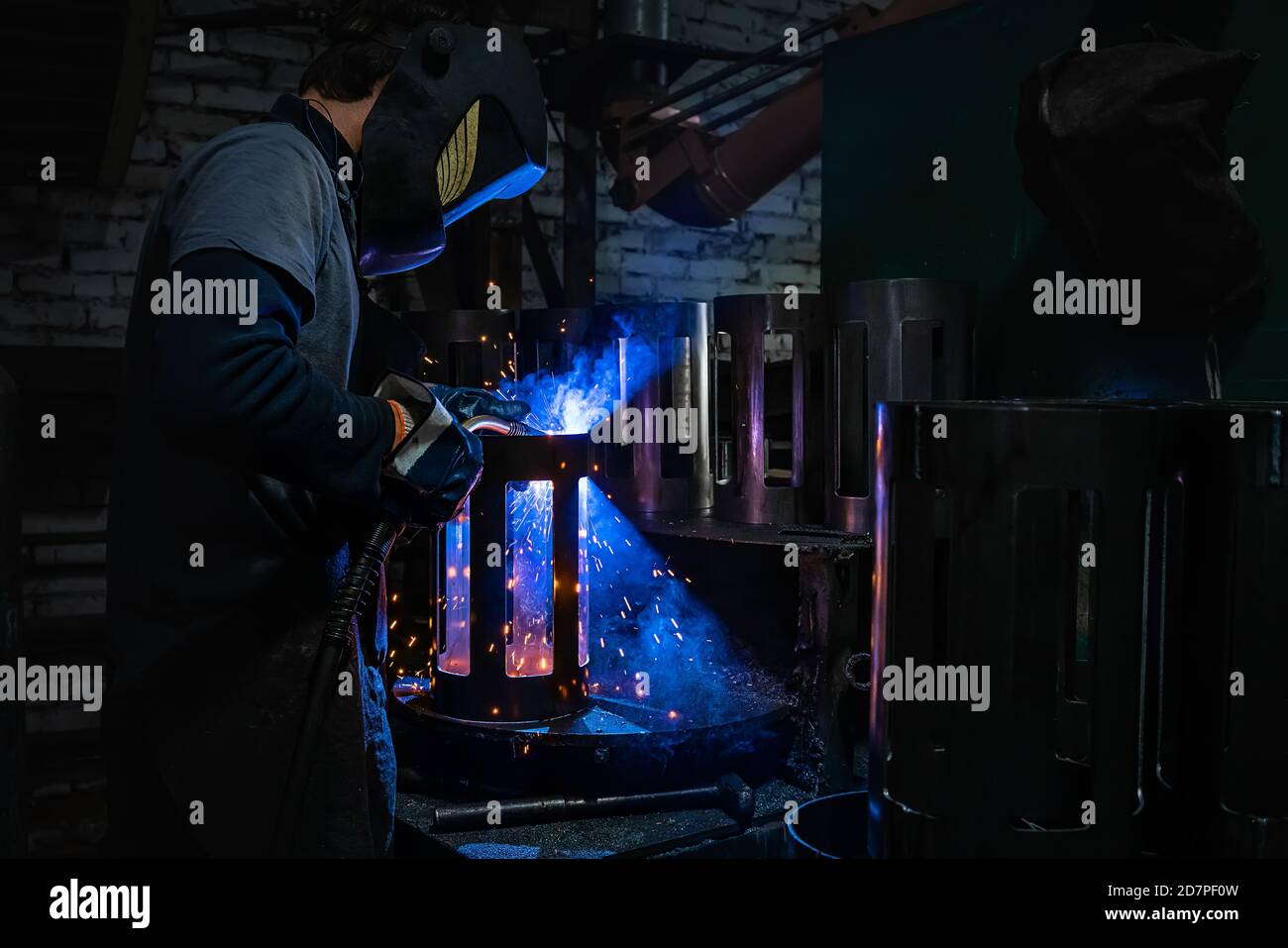 Side view of welder in protective helmet welding metal detail with sparks at factory Stock Photo