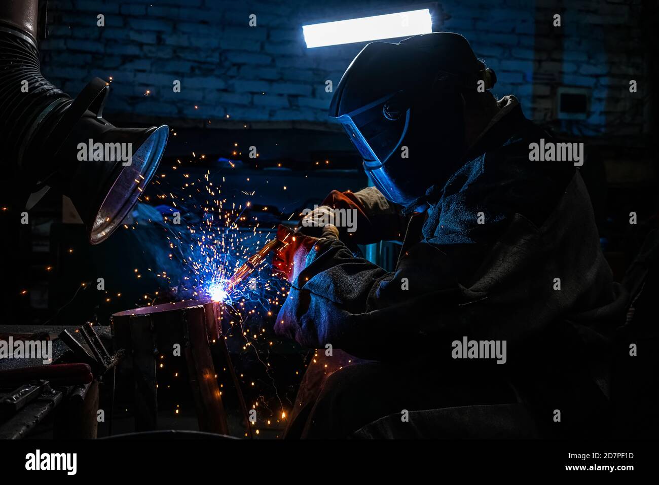 Side view of welder in protective helmet welding metal detail with sparks at factory Stock Photo