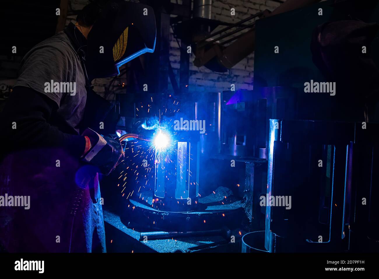 Side view of welder in protective helmet welding metal detail with sparks at factory Stock Photo