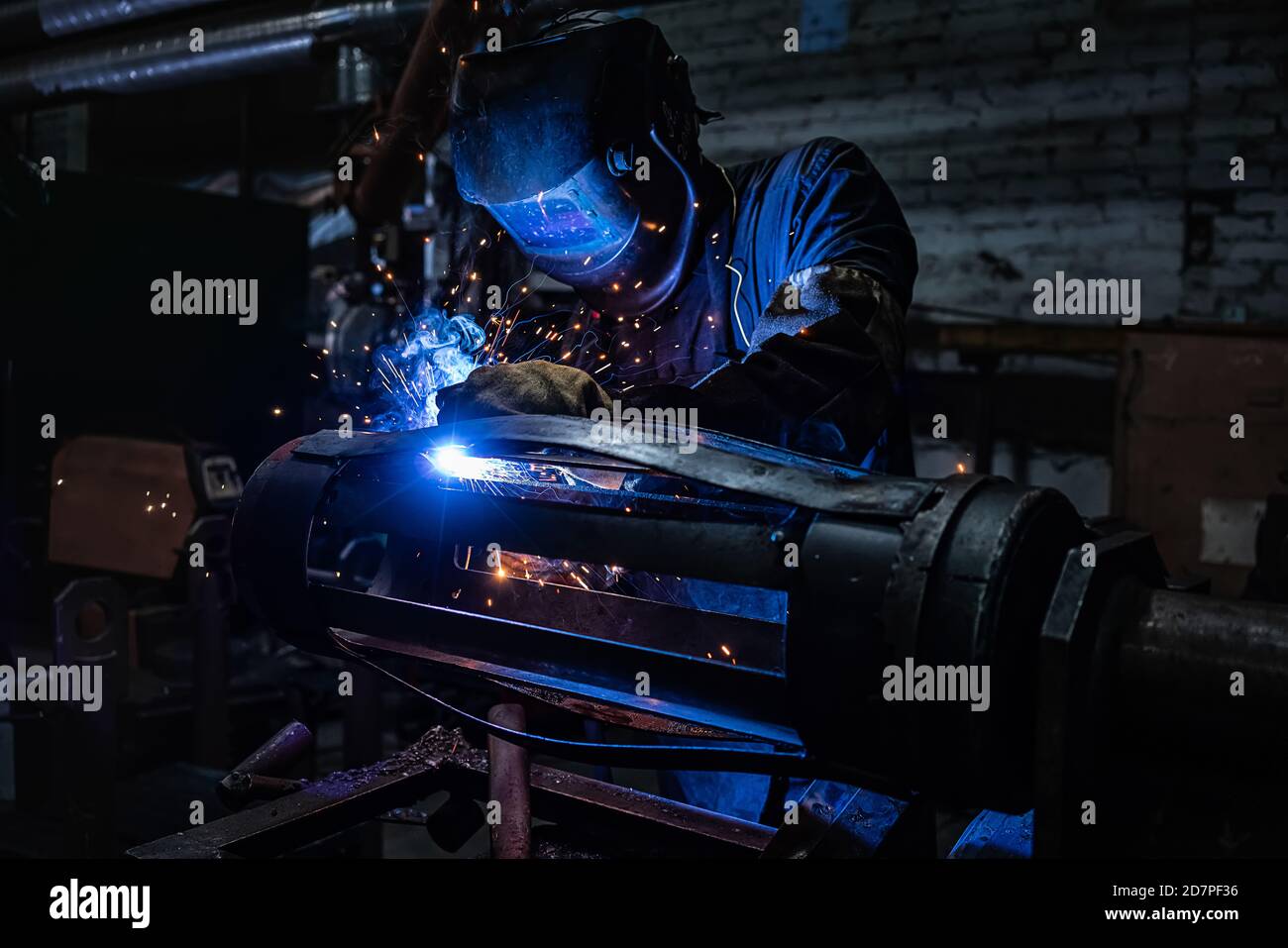 Side view of welder in protective helmet welding metal detail with sparks at factory Stock Photo
