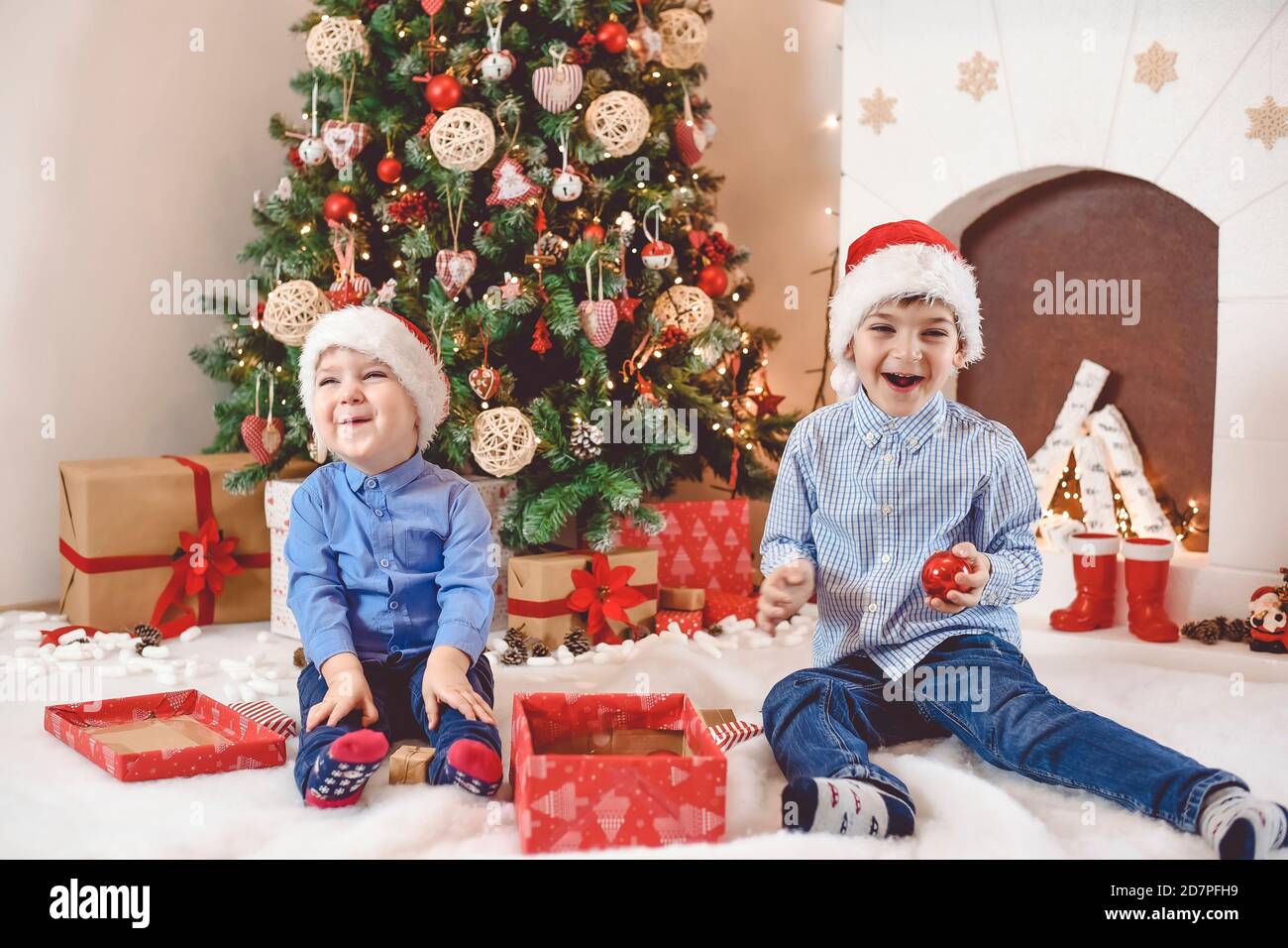 Happy and cute kids sit in front of the Christmas tree open presents and have fun Stock Photo