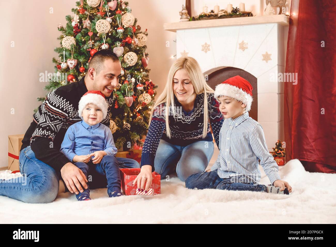 Mother, father and kids celebrate Christmas - they sitting in front of Christmas tree, playing and opening gifts Stock Photo