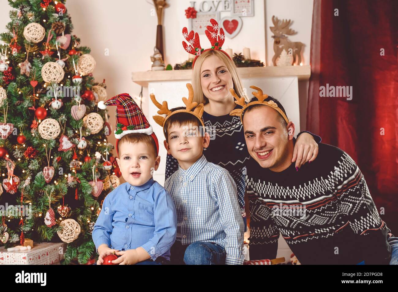 Mother, father and kids celebrate  sitting in front of Christmas tree, playing and opening gifts - Happy family celebrate Christmas - Family photo Stock Photo