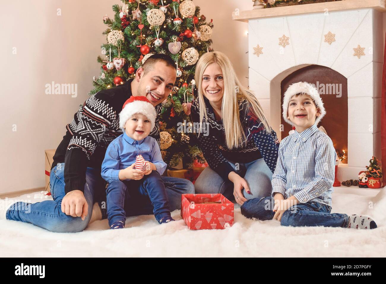 Mother, father and kids celebrate  sitting in front of Christmas tree, playing and opening gifts - Happy family celebrate Christmas Stock Photo