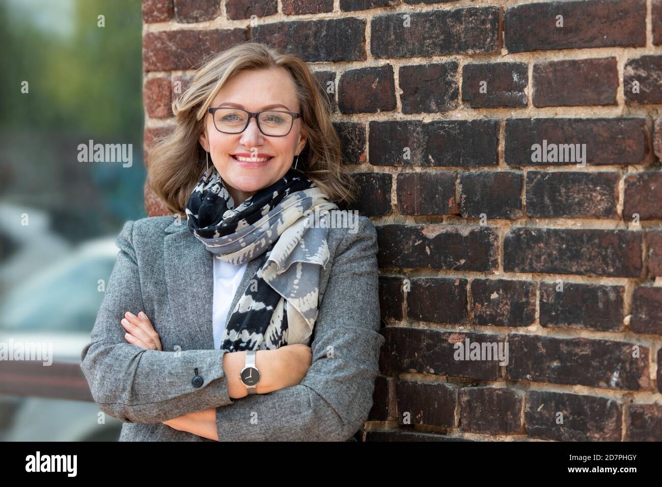 Portrait of a happy beautiful woman, 55 years old, smiling. On the street in the city, on the background of the old wall of red brick. Stock Photo