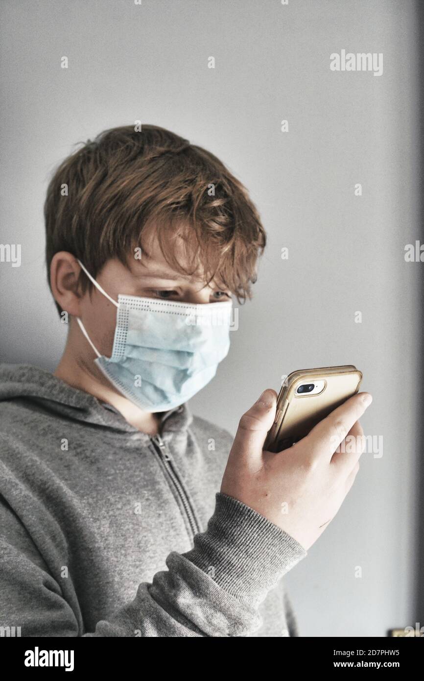 Teenage boy using his smartphone in surgical face mask Stock Photo - Alamy