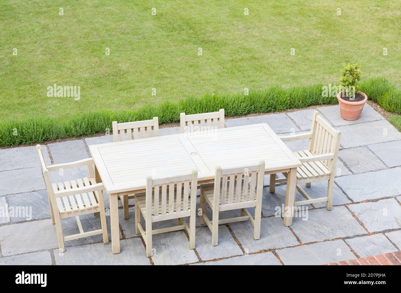 Wooden garden furniture on a patio terrace in a UK back garden with lawn Stock Photo