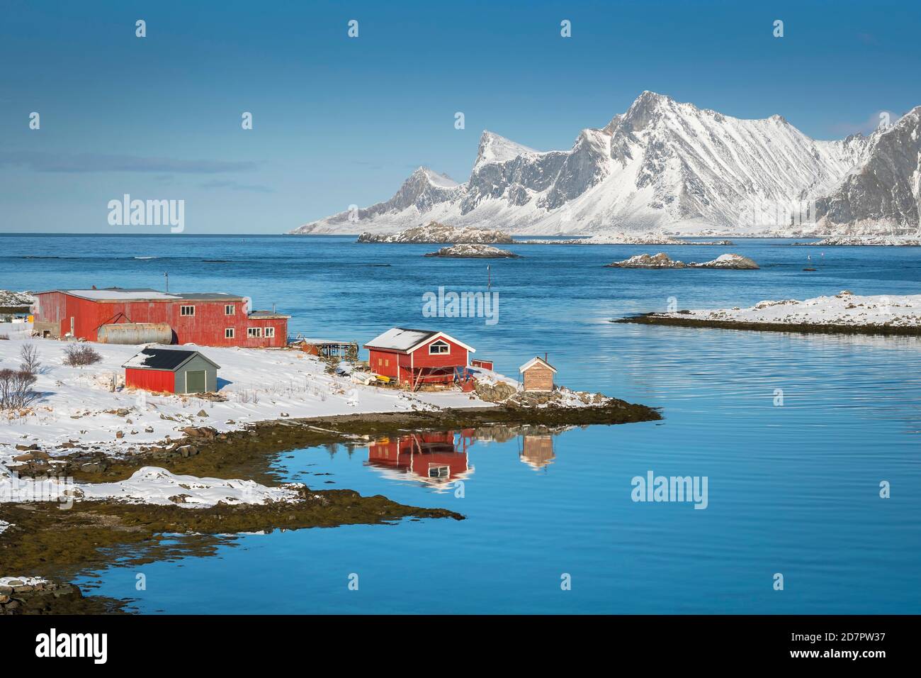 Red farmhouse reflected in the fjord Rossoy Straumen, in the back far ocean, snowy mountains Hustinden and Bjoerntinden, Nordland, Lofoten, Norway Stock Photo