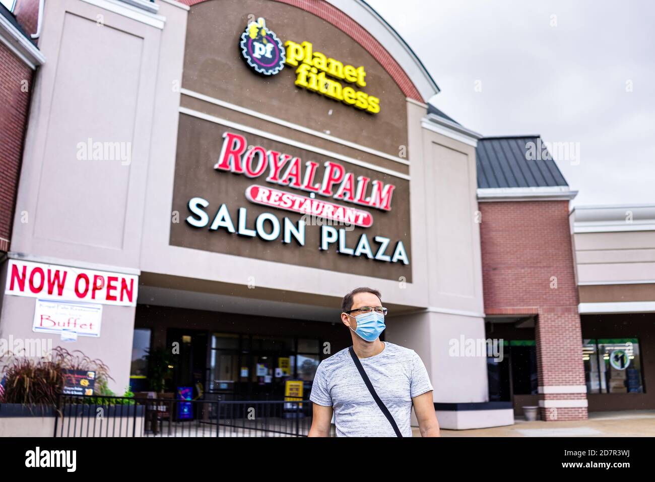 Sterling, USA - September 9, 2020: Stores at strip mall plaza with people man person in mask by planet fitness sign and now open during coronavirus in Stock Photo