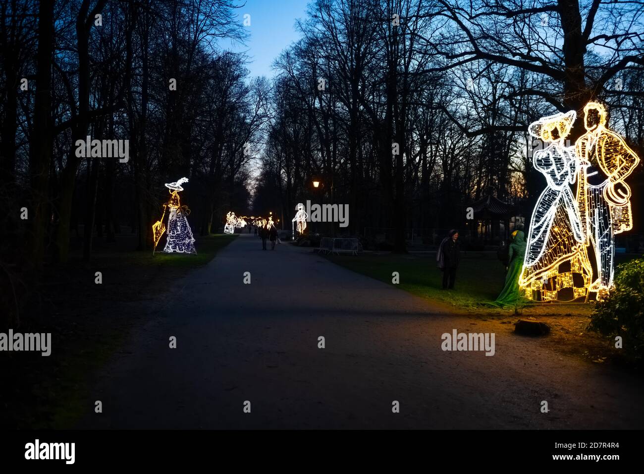 Warsaw, Poland - December 20, 2019: Illuminated decoration lights garland of couple statue at night evening at Christmas in Lazienki park with people Stock Photo