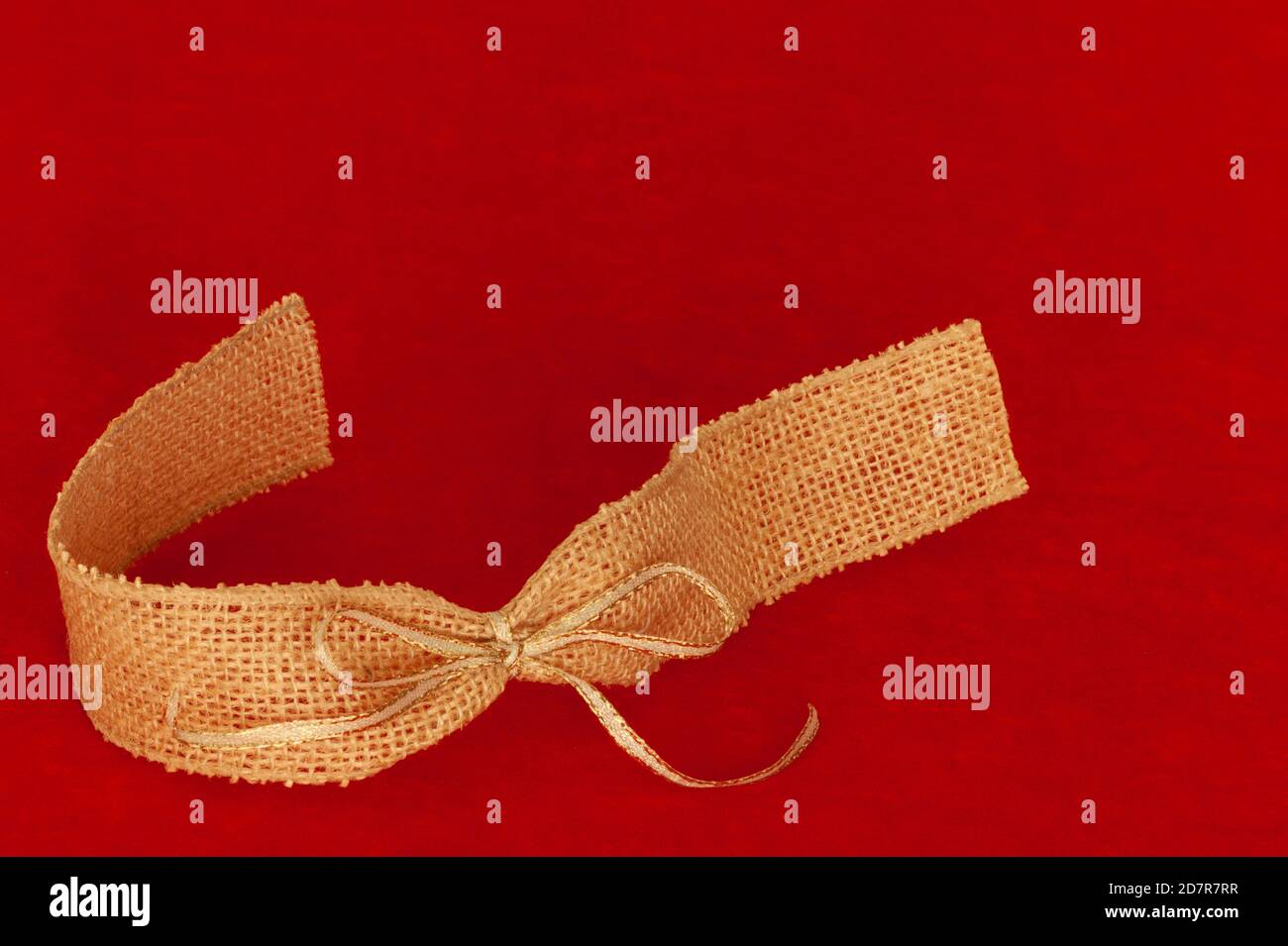 Gold and beige ribbon and bow on red fabric background with text space for message. Stock Photo