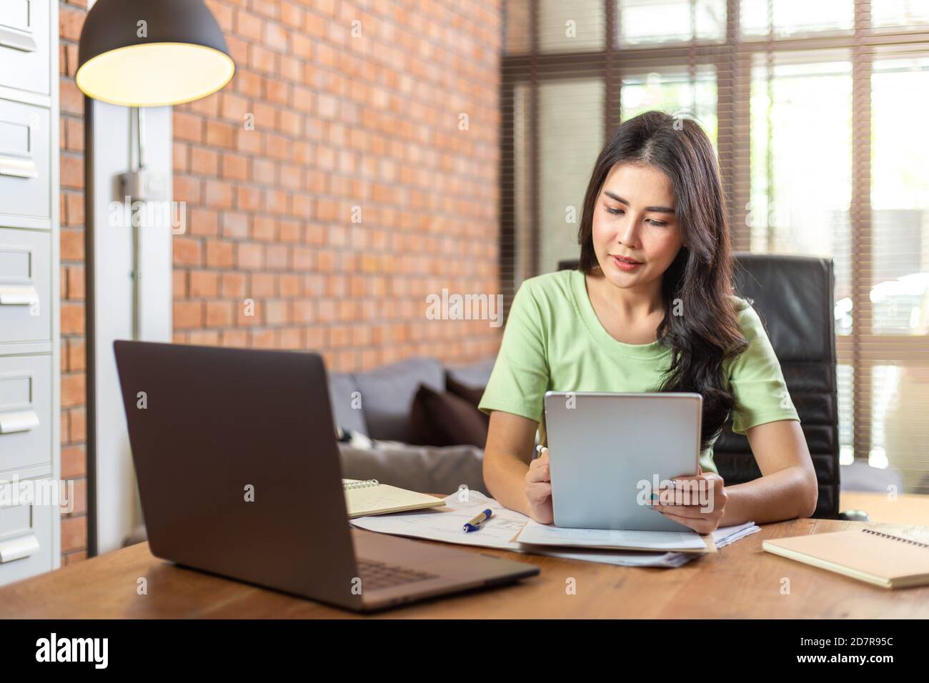 Young beautiful Asian business woman using a computer tablet while working from her home office during COVID pandamic lockdown Stock Photo