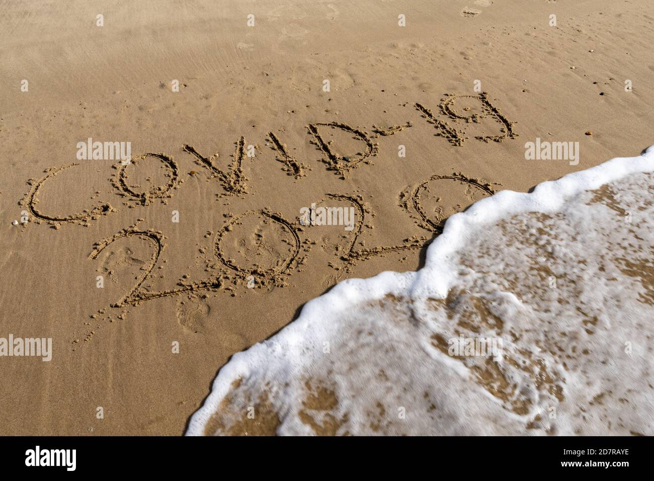 View of Covid-19 and 2020 text in sand on beach is covered by ocean wave and disappears Stock Photo