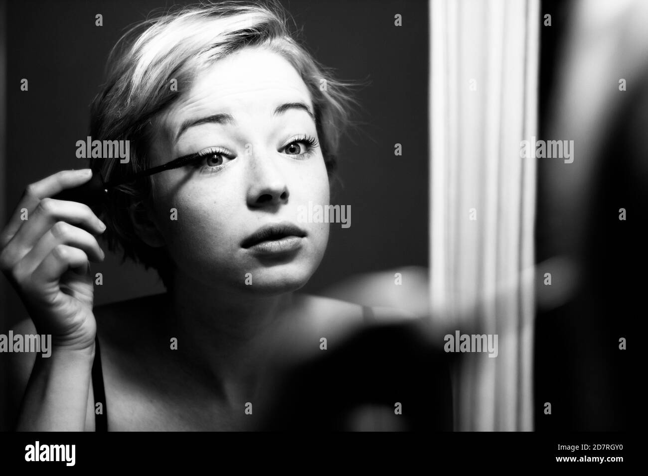 Woman getting ready for work doing morning makeup routine applying mascara in bathroom mirror at home. Beautiful caucasian girl applying eye make-up Stock Photo