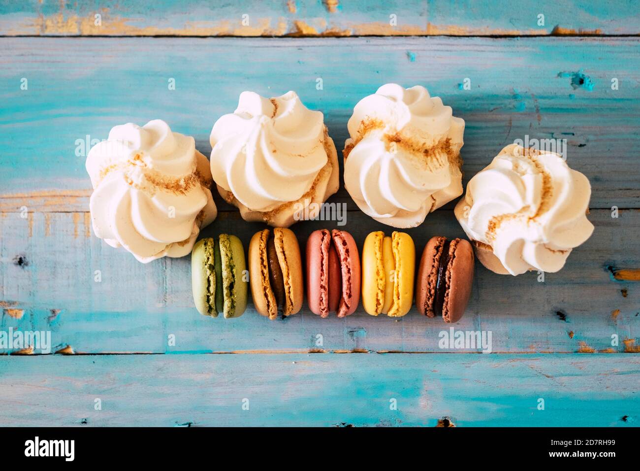 Top view of sweet cakes and macarones with sugar on a blue wooden table - Stock Photo