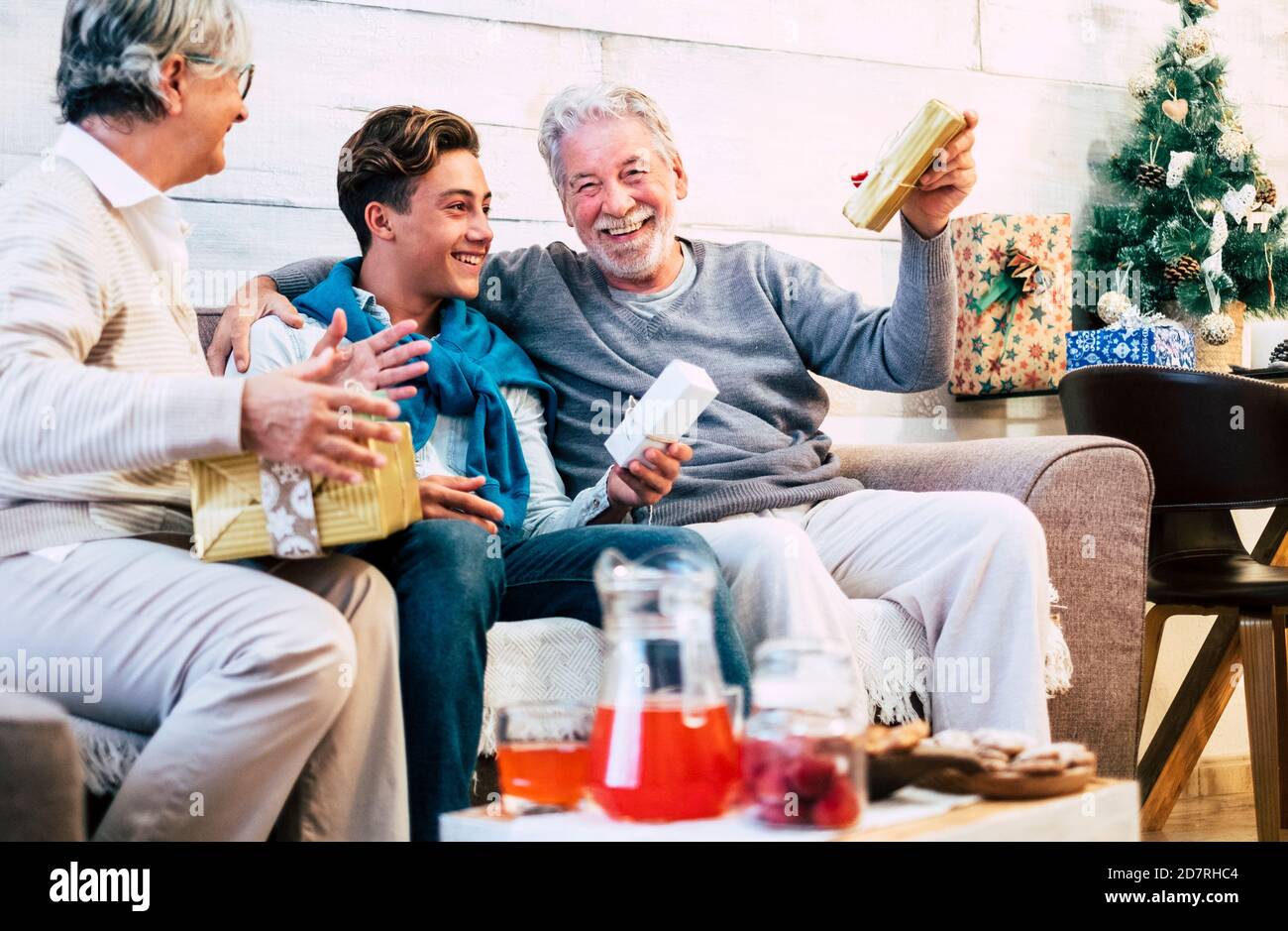 Happy cheerful family celebrate holiday and christmas eve together having fun and sharing gifts - young boy with senior old grandfathers have fun with Stock Photo