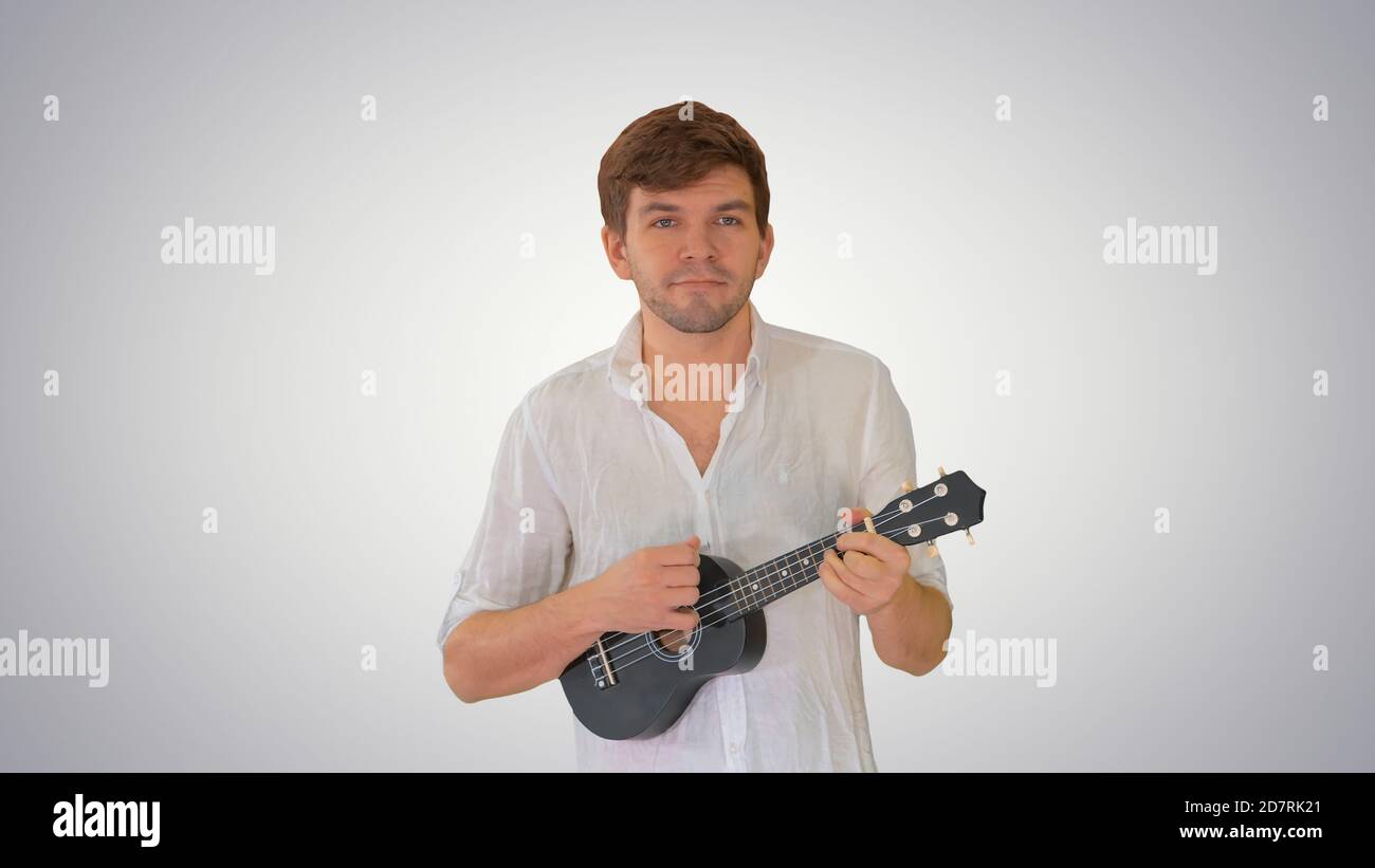 Young man playing ukulele while walking on gradient background. Stock Photo