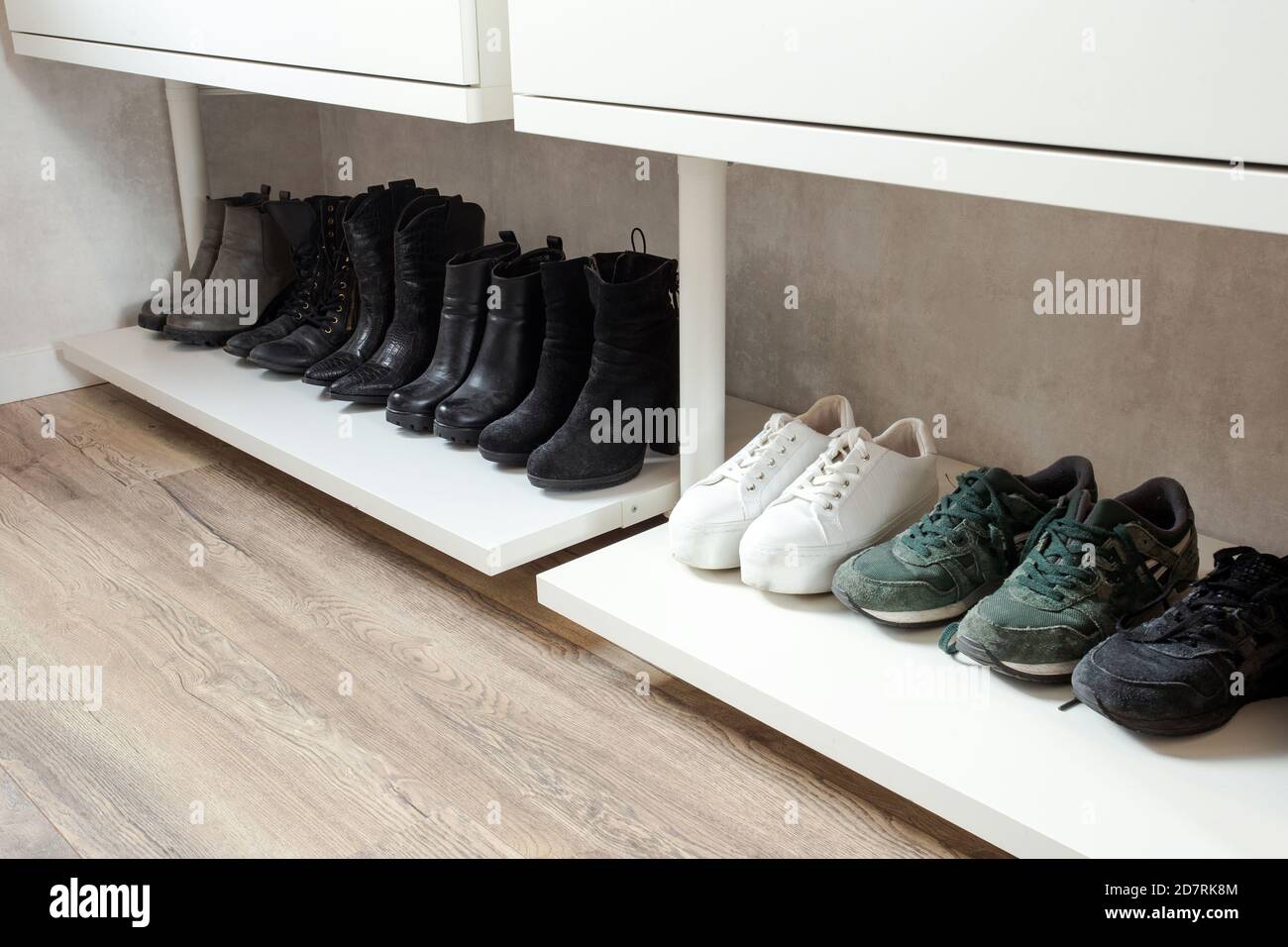Organized shoe rack, shoe rack with black stylisch shoes and boots, on a wooden floor, besides a white wall. modern room Stock Photo