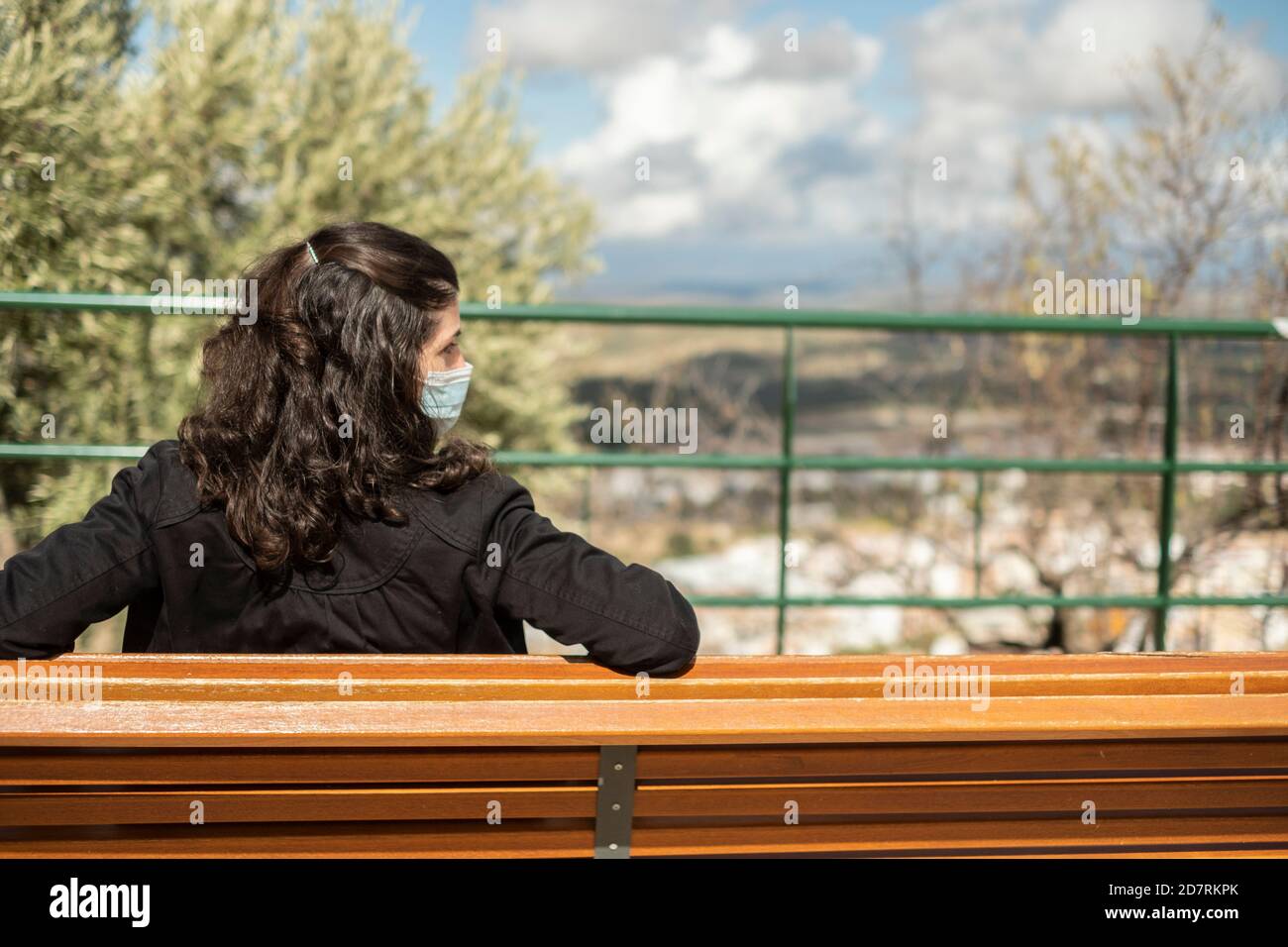 Woman sitting on a bench on cloudy day with surgical mask rests alone Stock Photo