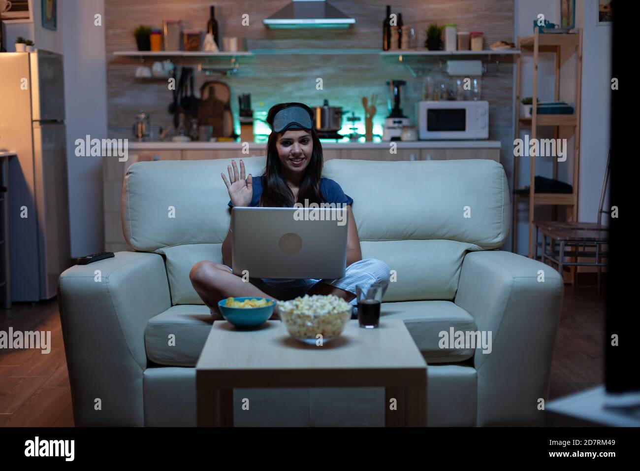 Lady with eye mask having video calling on laptop computer at night.  Exhausted person in pijamas