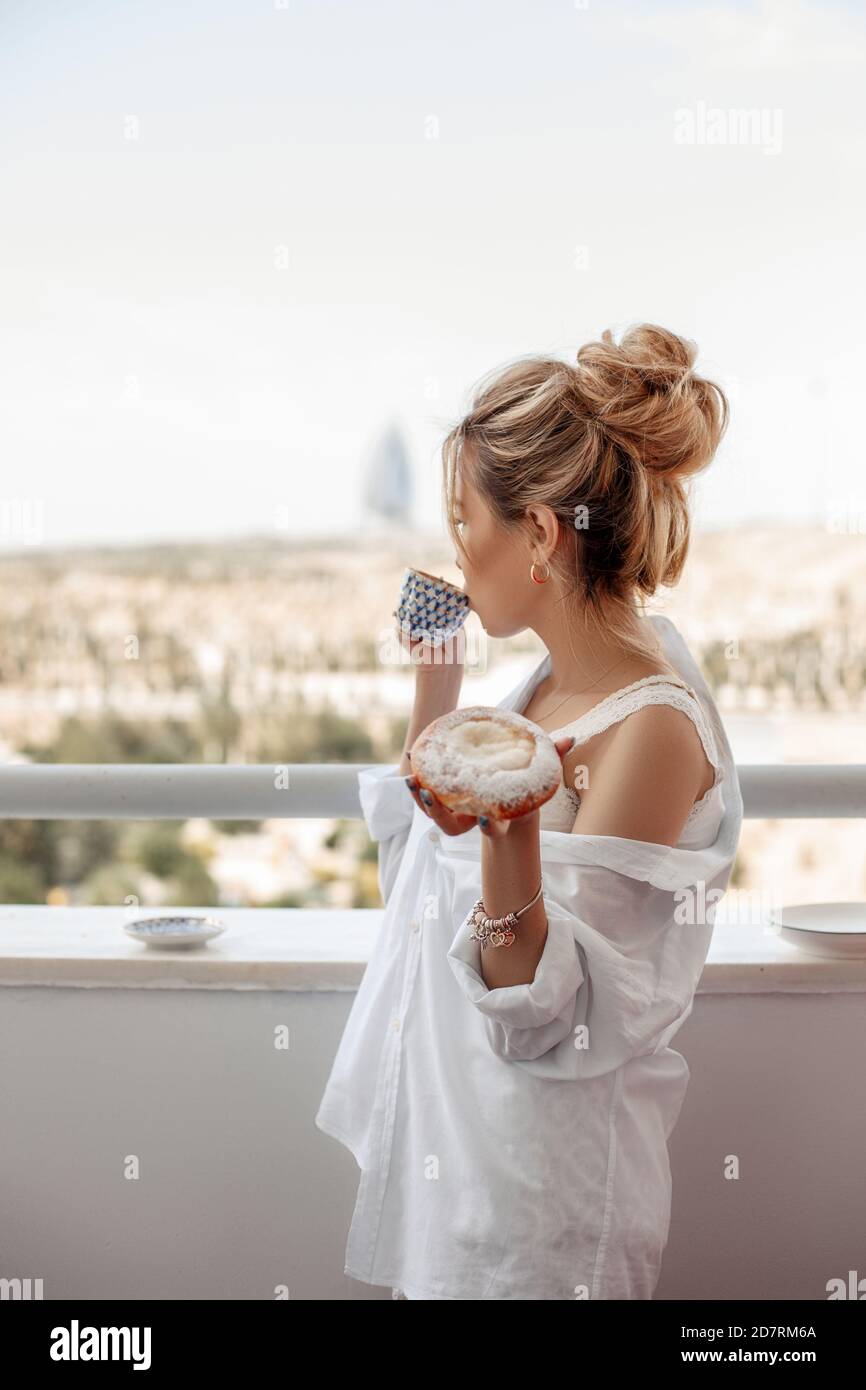 young beautiful Asian girl in beige lace shorts,white shirt eating dessert, pie on the balcony. selective focus. small focus area. Stock Photo