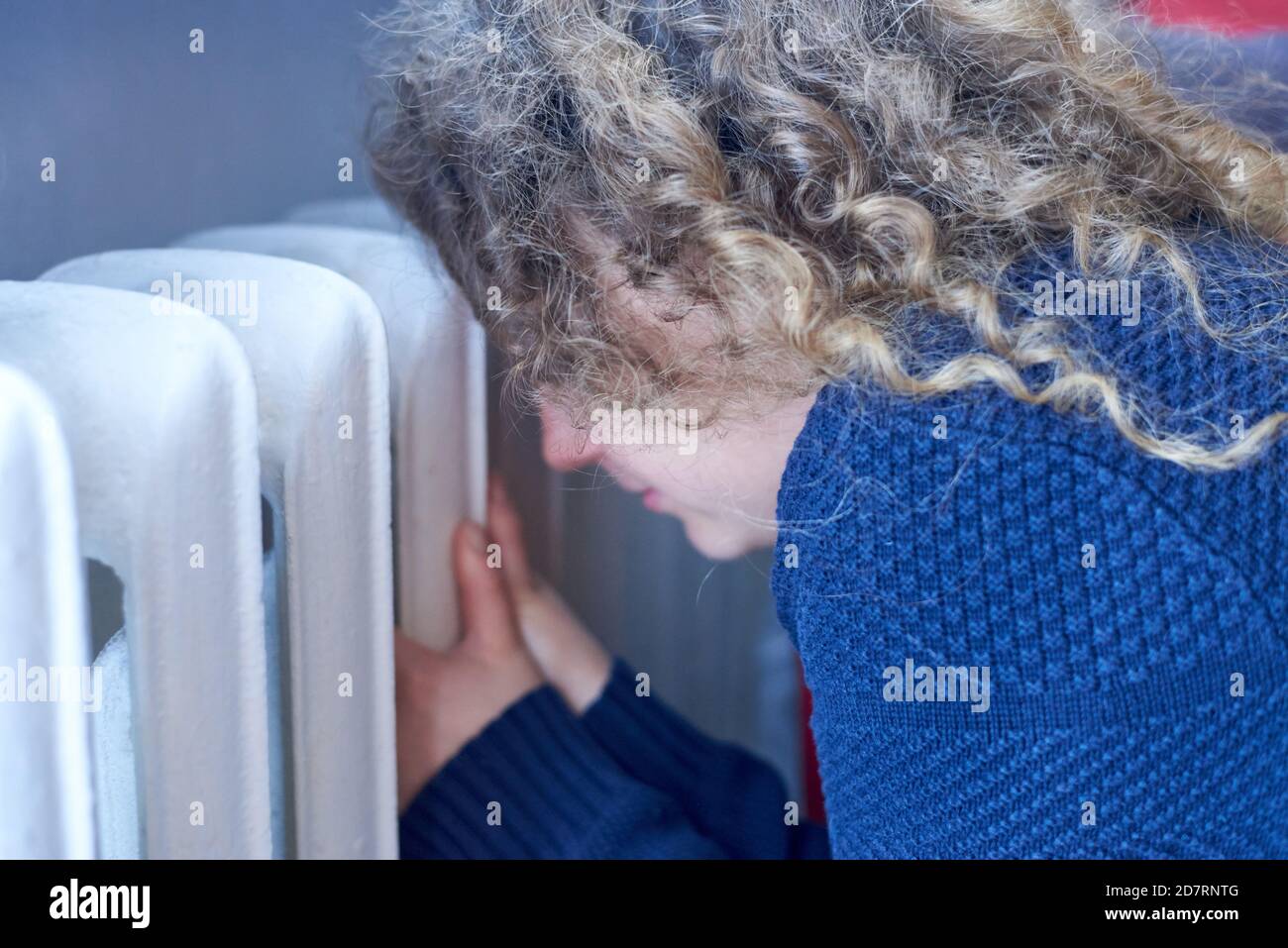 The woman keeps her hands on the radiator and warms up, heating season
