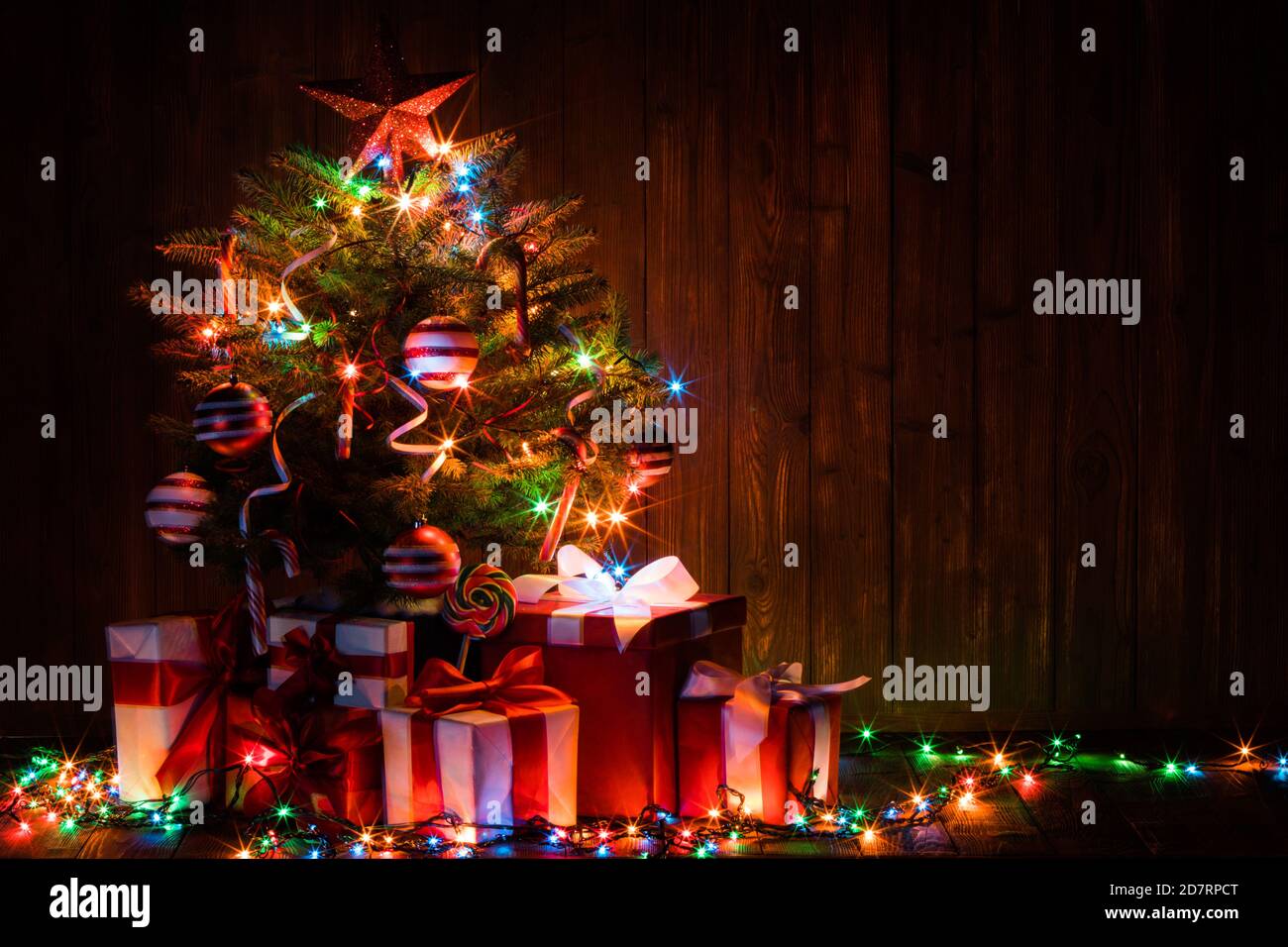 Decorated lighted Christmas tree and gift boxes on wooden background Stock Photo