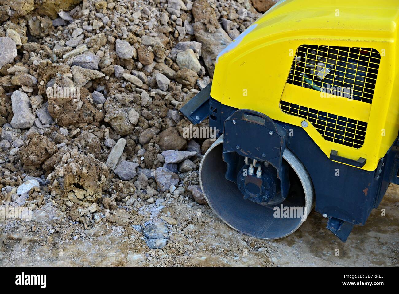 Background detail of a yellow road roller during stone paving. Rolled soil and stones. Substrate preparation for a new road. Steel industrial roller f Stock Photo