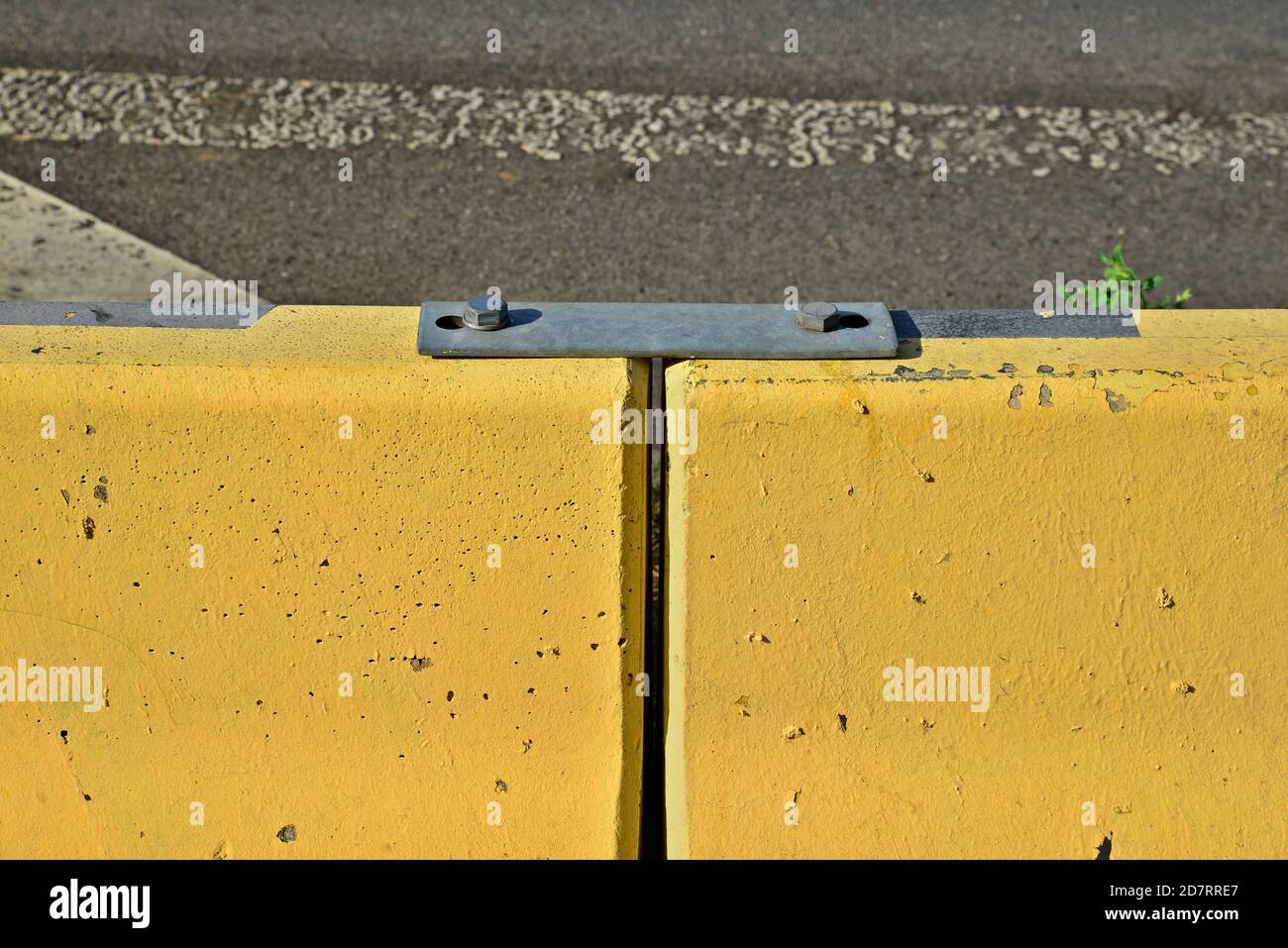 Two yellow concrete blocks connected by a steel coupling. Jersey barrier, Jersey wall, modular concrete barrier employed to separate lanes of traffic. Stock Photo