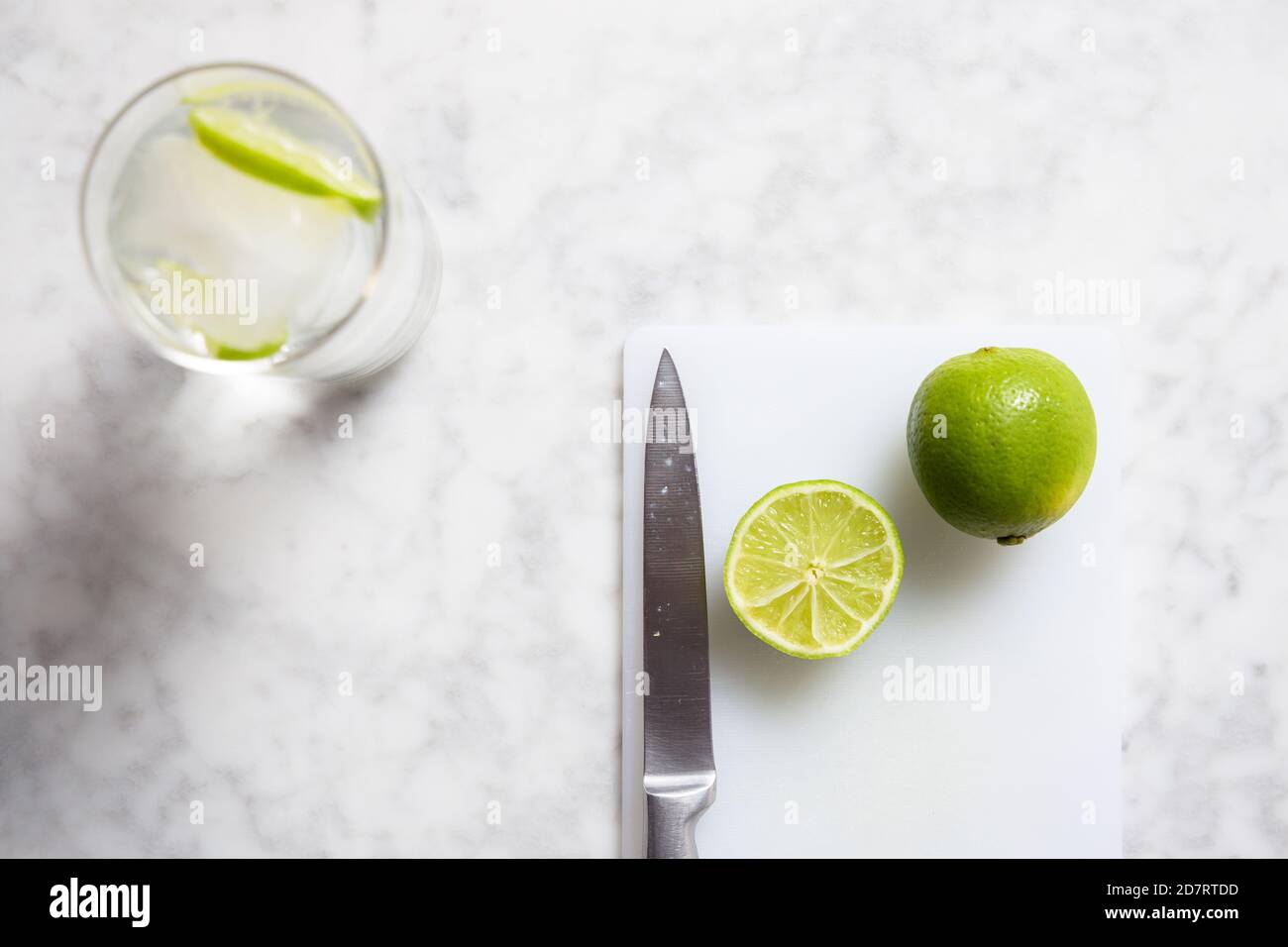 Top view of a gin tonic, a knife and two limes on a marble table. Gin