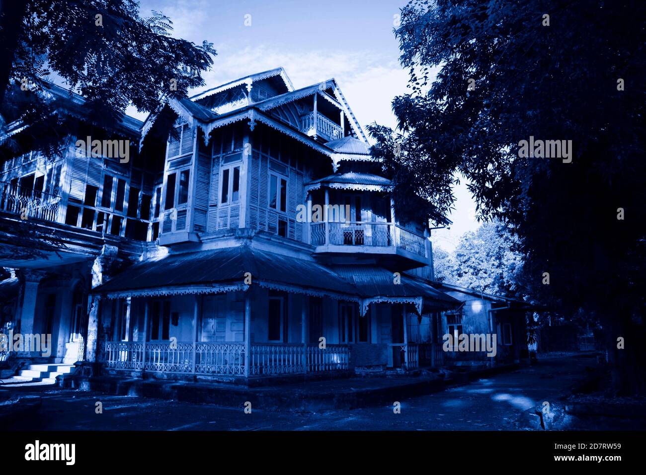 Haunted House with Dark Horror Atmosphere. Scary colonial cottage in mysterious forestland. Photo toned in blue color Stock Photo
