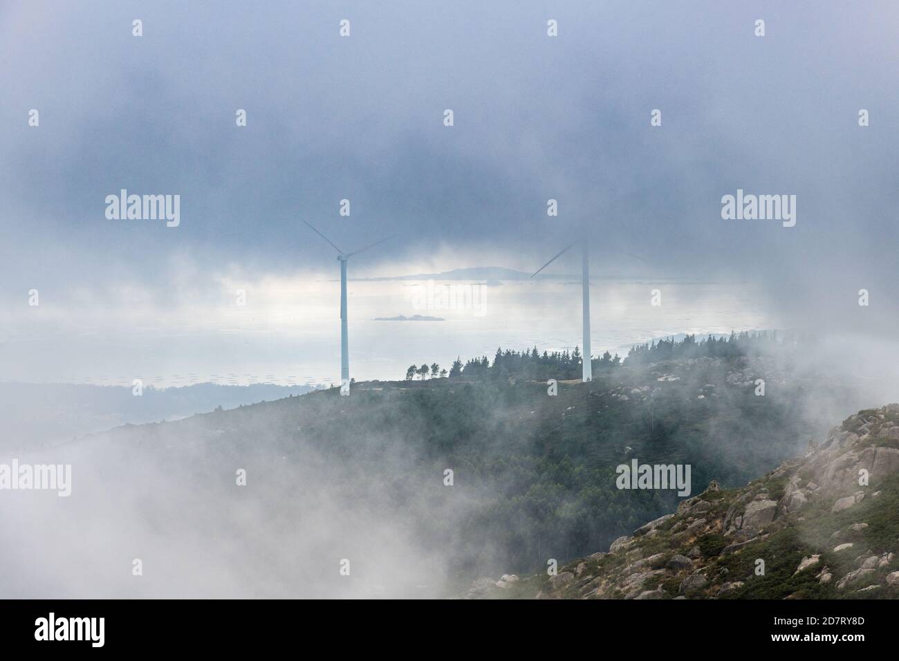 Aerial view of the Ria de Arousa estuary from the Muralla mountain on a foggy Summer afternoon, with some wind turbines among the clouds. Stock Photo