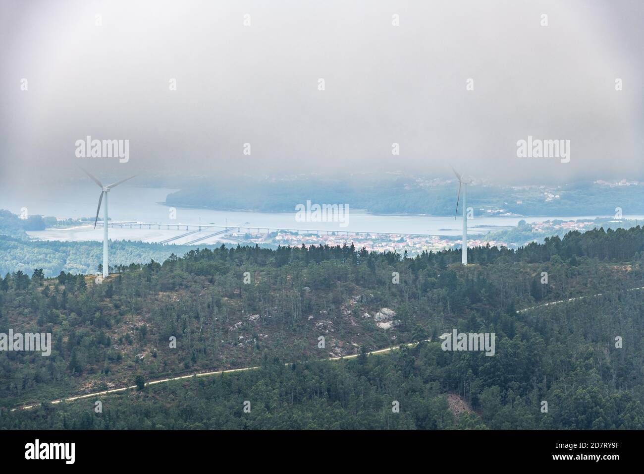 Aerial view of the Ria de Muros y Noya estuary from the Muralla mountain on a foggy Summer afternoon, with some wind turbines among the clouds. Stock Photo