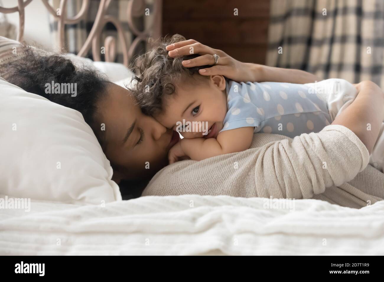 Loving biracial mom lying in bed with little baby Stock Photo