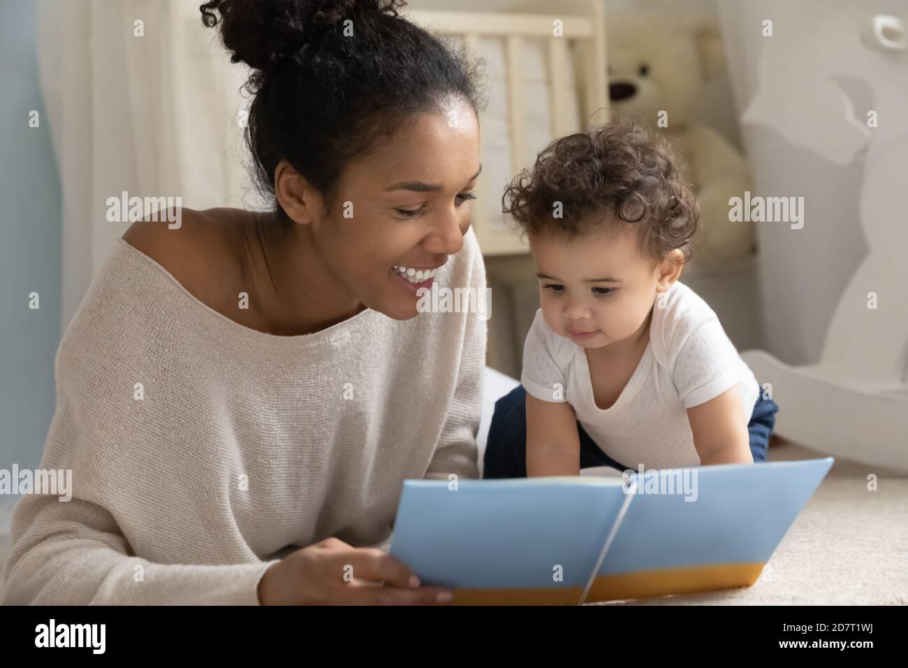 Smiling biracial mom read book with baby infant Stock Photo