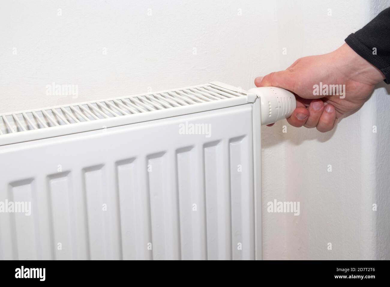 Male hand regulates the thermostat knob on the white heating radiator ...