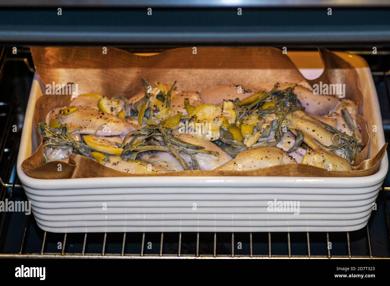 Chicken grilling in an oven with sage and lemon peels Stock Photo