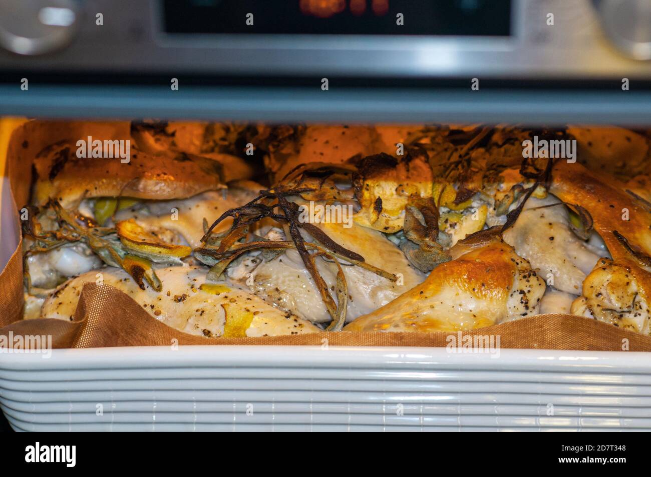 Chicken grilling in an oven with sage and lemon peels Stock Photo