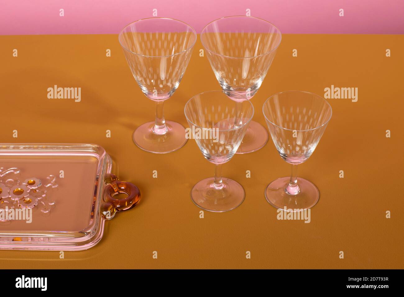 Set of classsic martini cocktail glasses standing next to a glass serving plate on a brown surface and a pink background. Clean minimalistic elegant s Stock Photo