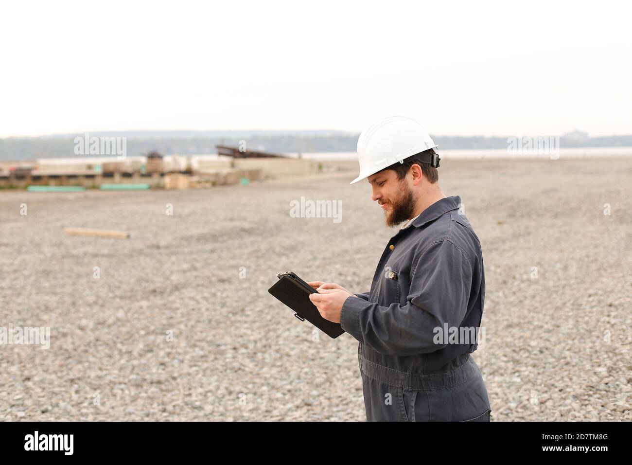Foreman in helmet surfing internet by tablet on construction site. Stock Photo