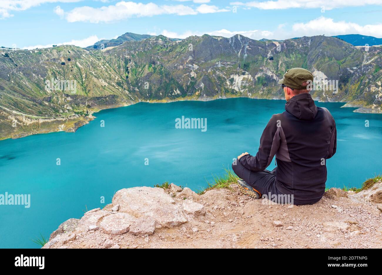 Young male backpacker with landscape of the Quilotoa volcanic lake on the highest peak at 3930m altitude along the Quilotoa Loop hike, Quito, Ecuador. Stock Photo