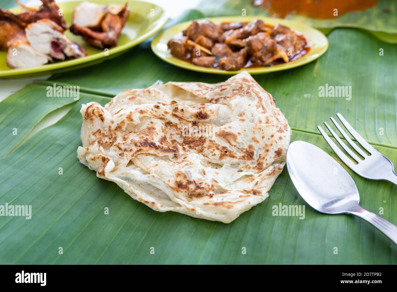 Roti canai or paratha served on banana leaf, with mutton curry and fried chicken Stock Photo