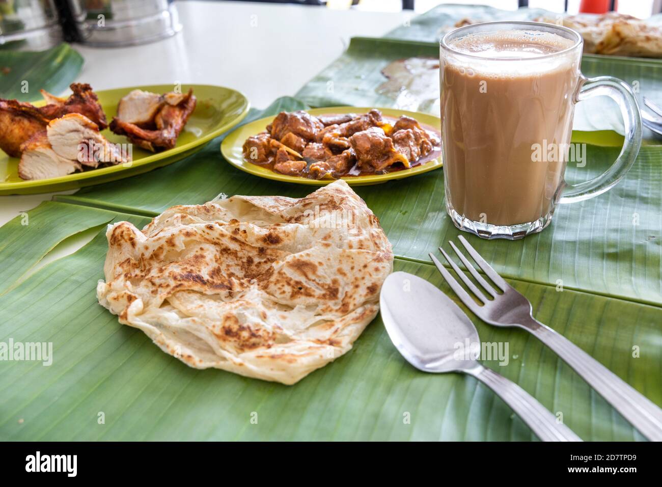 Roti canai or paratha served on banana leaf, with mutton curry and fried chicken, and popular teh tarik Stock Photo