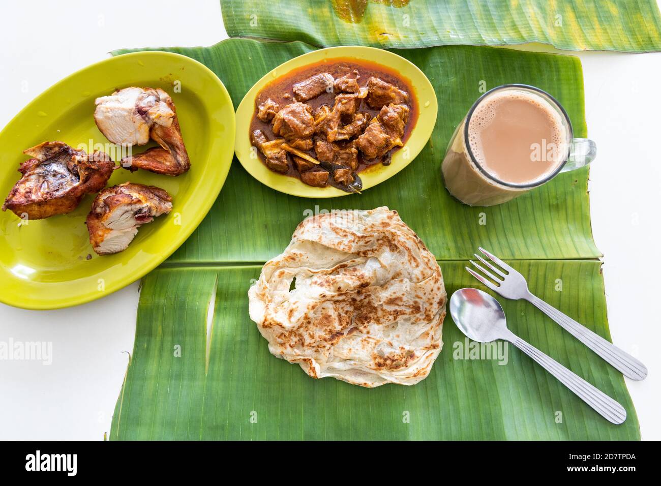 Overhead view of roti canai or paratha served on banana leaf, with mutton curry and fried chicken Stock Photo