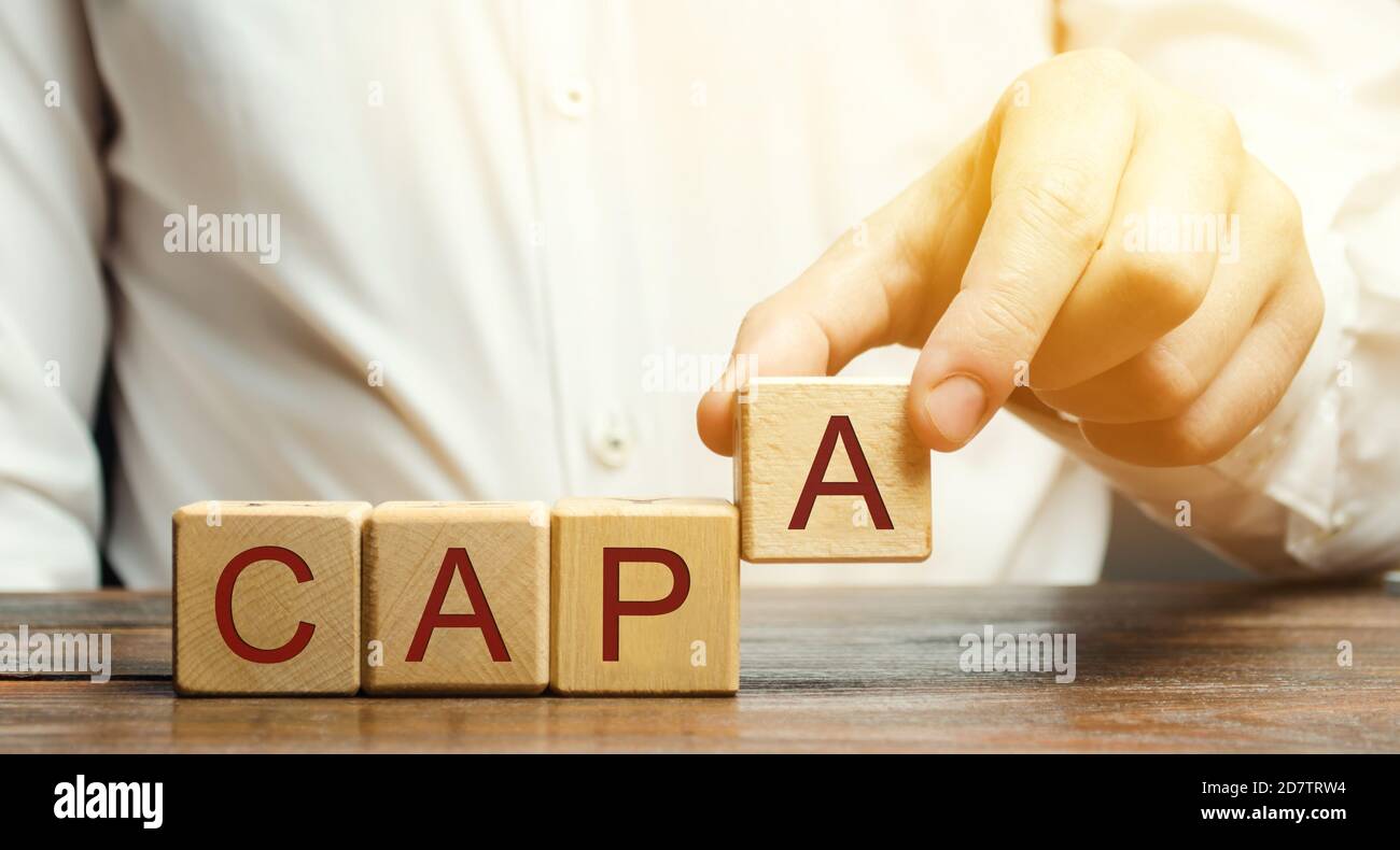 Businessman puts wooden blocks with the word CAPA. Corrective and Preventive action plans. Business management concept. Strategy and efficiency. Impro Stock Photo