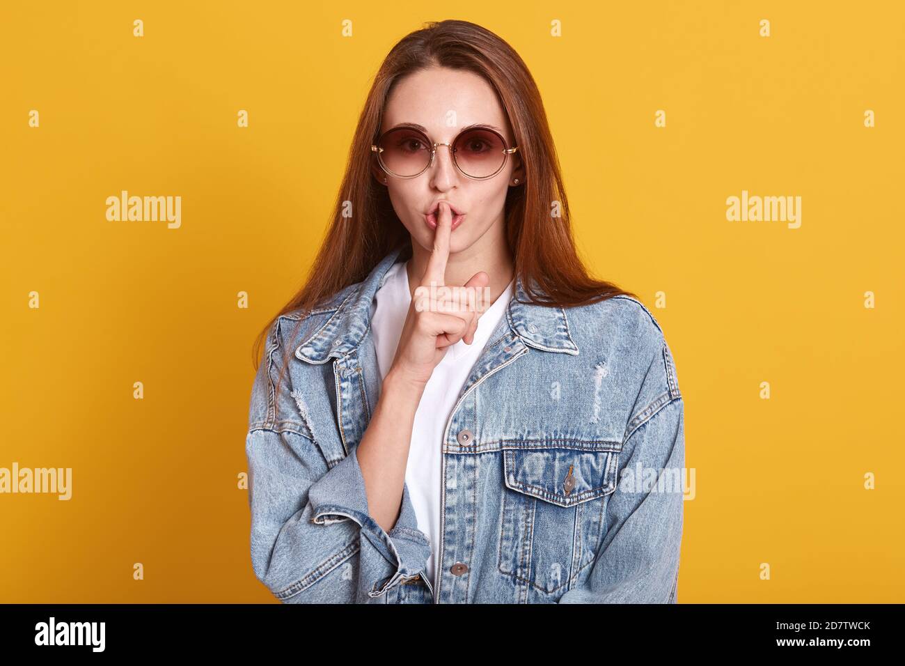 Portrait of mysterious stylish pretty model making gesture, putting her forefinger to lips, looking directly at camera, keeping secrets, wearing white Stock Photo