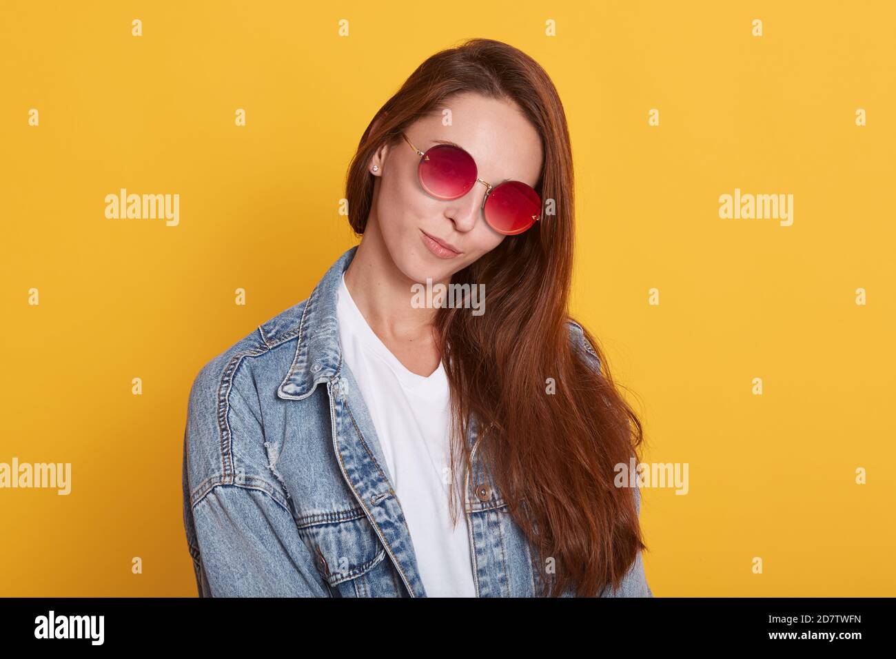 Close up portrait of attractive woman with dark hair, posing isolated over yellow studio background, winsome lady dresses denim jacket, white casual s Stock Photo