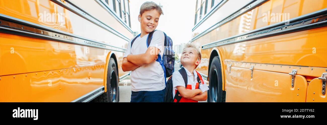 Happy Caucasian brothers students near yellow school bus. Smiling kids going back to school in September. Education system and learning. Support Stock Photo