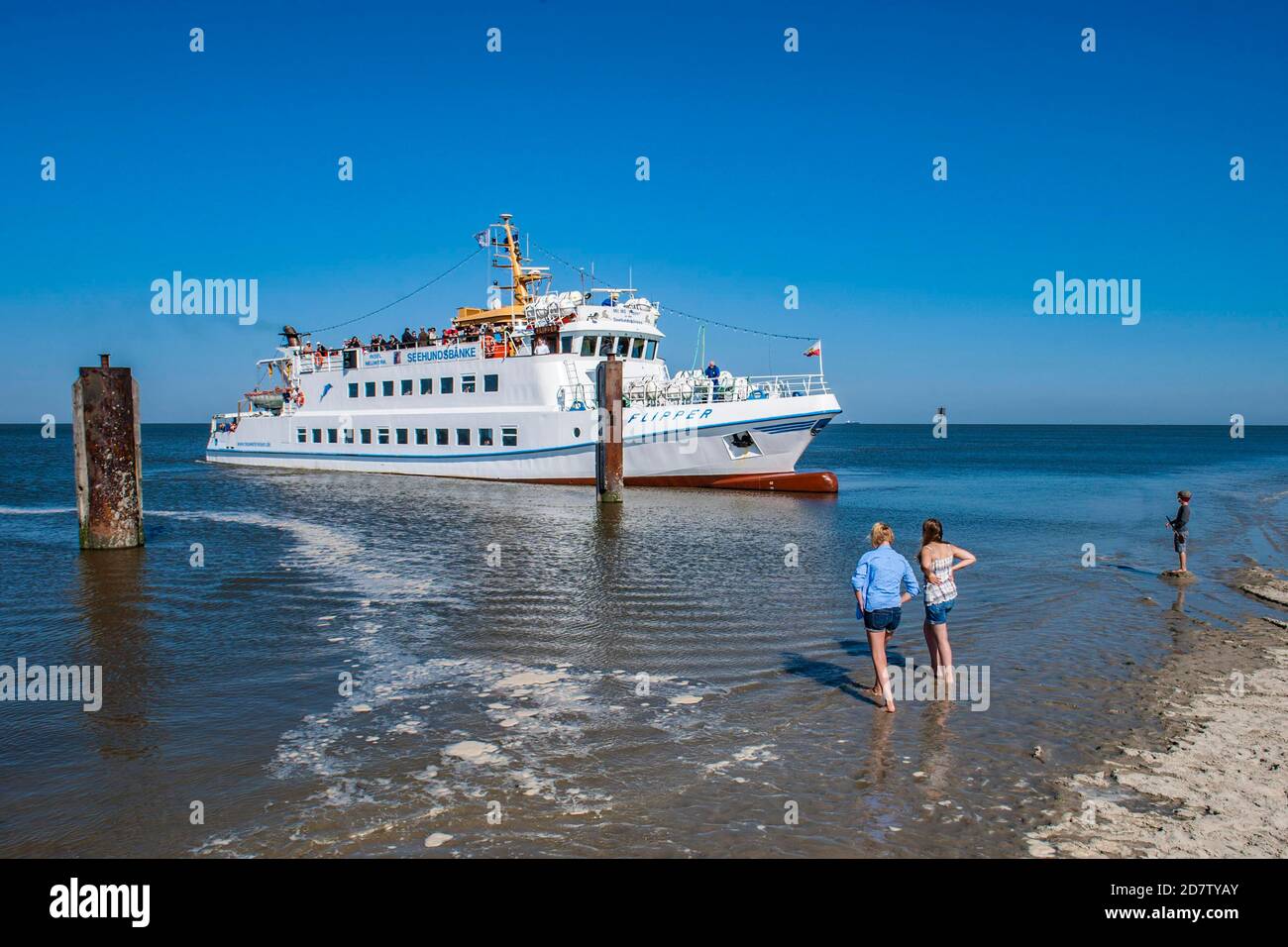GERMANY, ISLAND NEUWERK,  Ferry 'Flipper' approaching the pier of island Neuwerk at high tide with two girls and a boy watching from the be Stock Photo